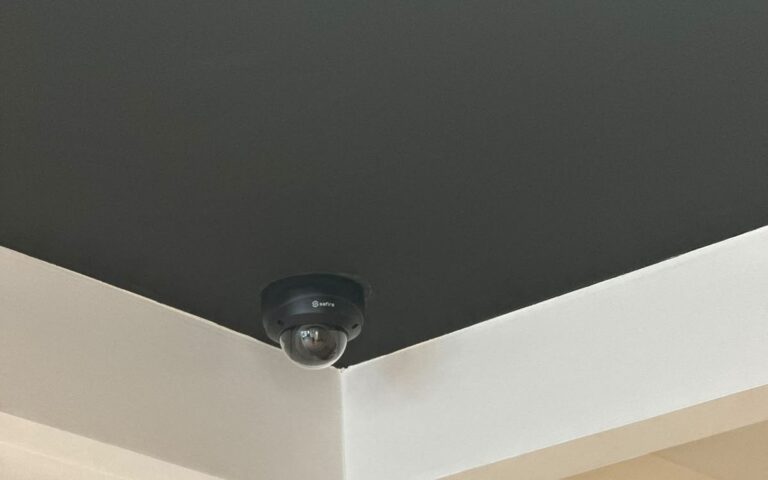 Kleine witte dome-camera tegen een wit plafond bij een doorgang