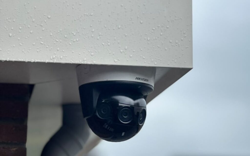 Zwarte PTZ-camera onder de dakrand van een woning, met de straat op de achtergrond