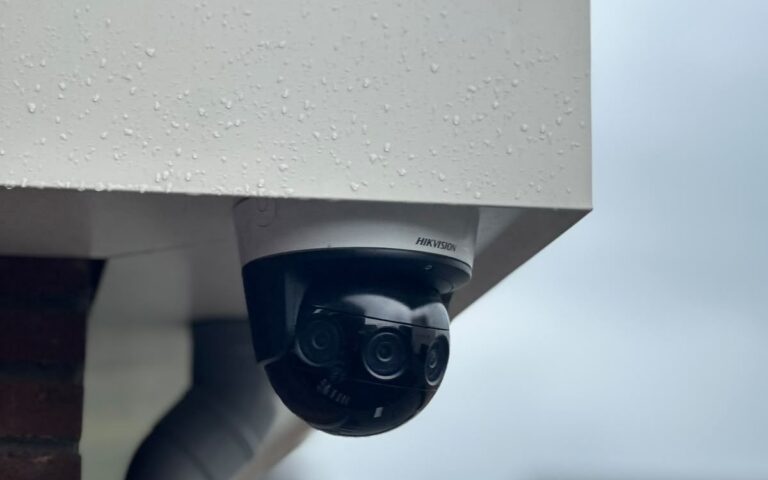 Zwarte PTZ-camera onder de dakrand van een woning, met de straat op de achtergrond